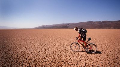 A man circunnavigating the globe rides a bike through a dry desert.