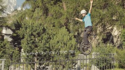 A man is extreme unicycling over a fence.