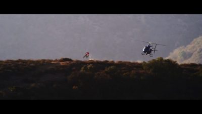 A helicopter hovers over a person riding a mountain bike on a hill in L.A.