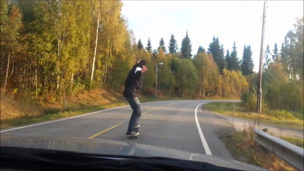 A person skateboarding down a road with trees in the background performs a skateboard manual.