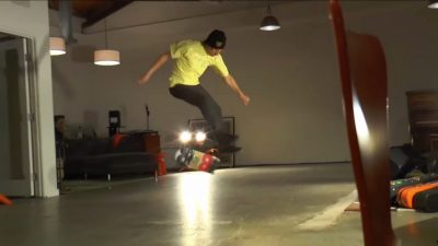 A skateboarder, performing a trick in a room, reminiscent of Rodney Mullen's style.
