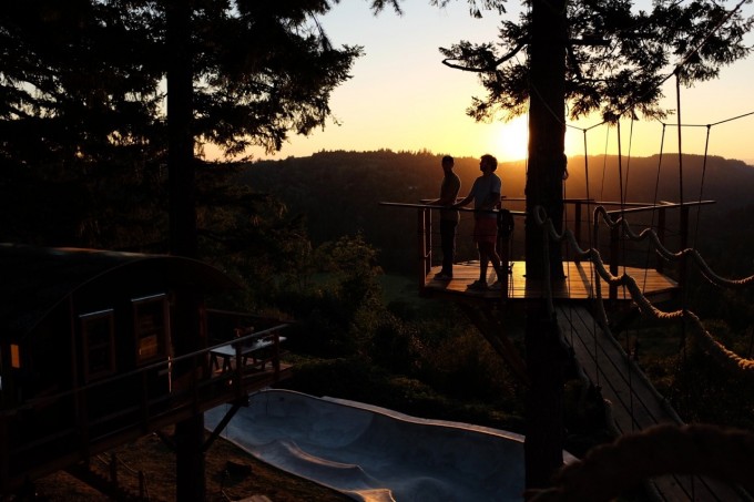 Two people standing in a treehouse and looking at a sunset