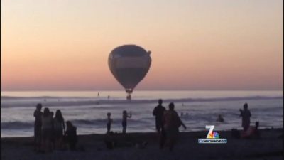 A hot air balloon floats gracefully over the beach at sunset, with passengers taking in the breathtaking view.
