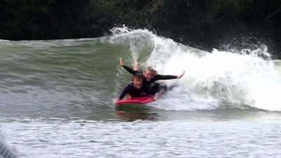 Two people riding a wave at Surf Snowdonia, an open-air Wavegarden attraction.