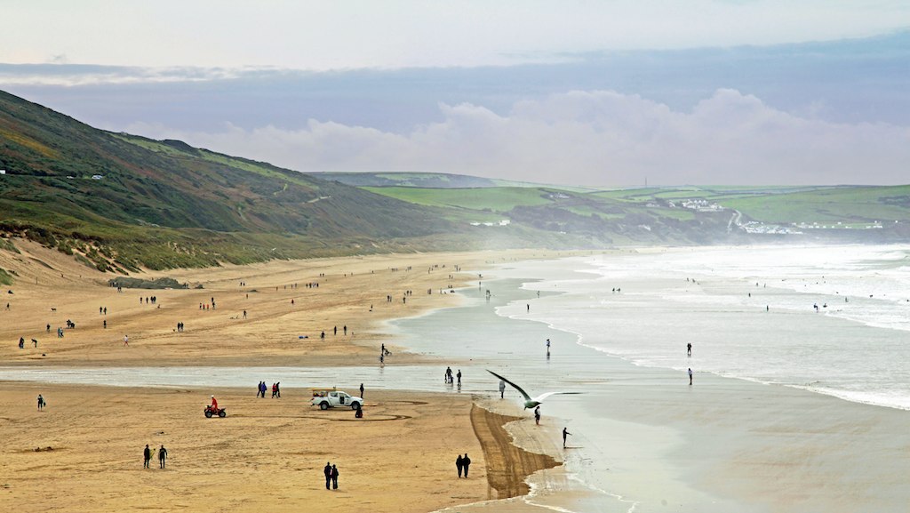 A crowded beach in Europe with people walking on the sand.