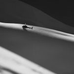 A black and white photo of a helicopter flying over a snowy hill captured by Valdez Heli Ski Guides.