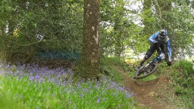 A man riding a mountain bike in the woods, representing his home country on the EWS circuit.