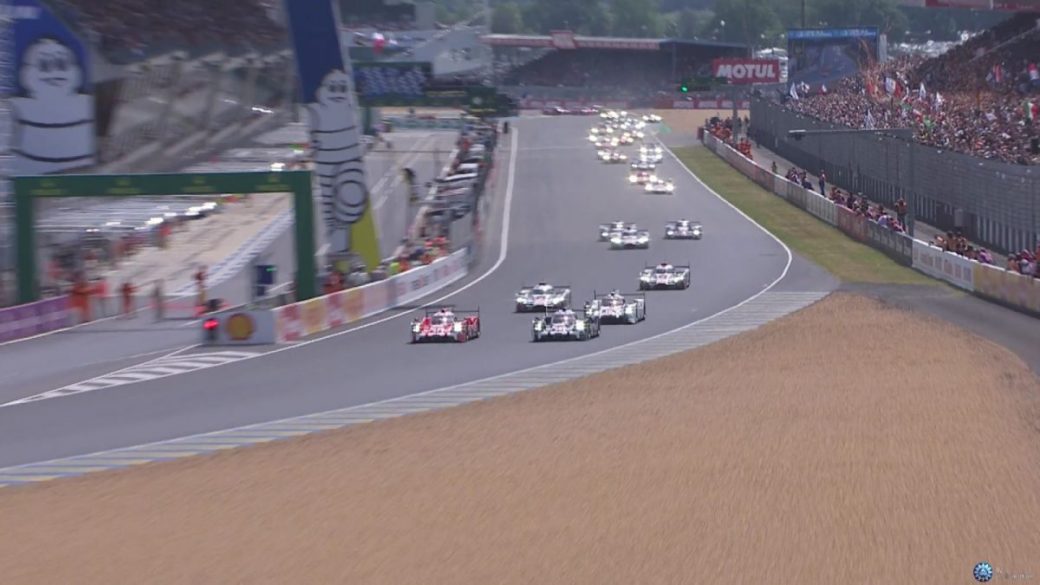 A group of race cars, including Porsche models, speeding down the track at Le Mans in 2015.