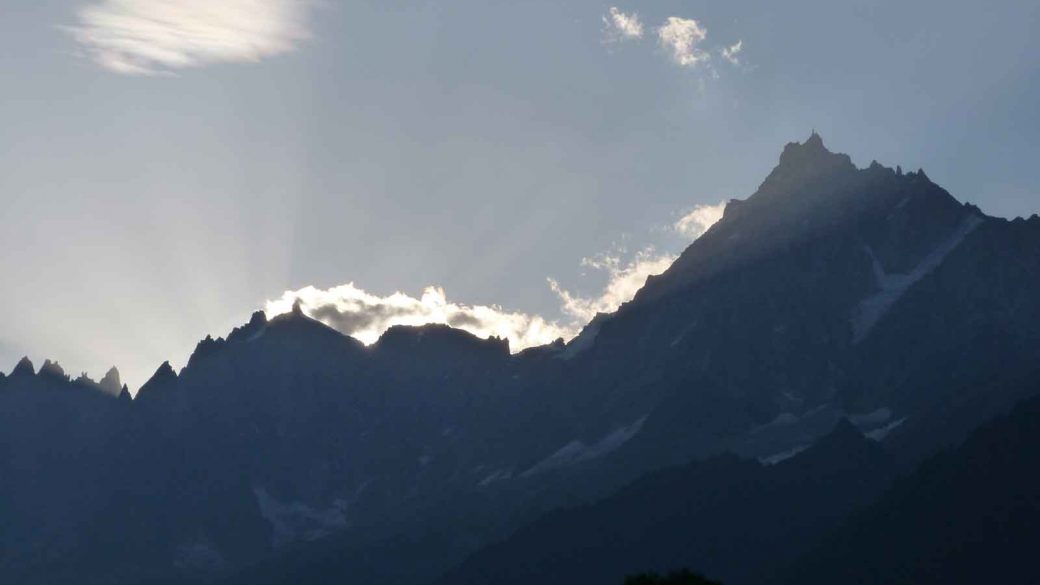 The sun shines through the clouds over a mountain range in Europe, creating a picturesque scene.