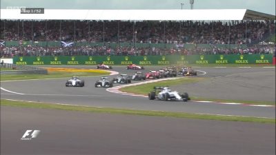Lewis Hamilton takes the lead in the British GP race, speeding down the track as a crowd watches in excitement.
