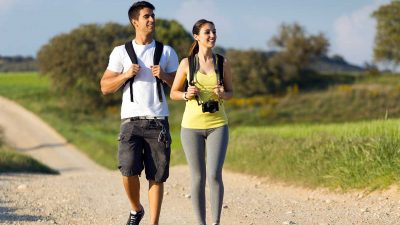 Man and woman wearing backpacks and trekking along a path