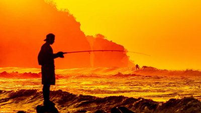 Silhouette of a man fishing at the beach during sunset