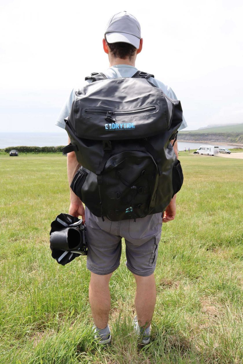 Looking out to sea and carrying the DryTide 50L waterproof backpack whilst holding a pair of flippers