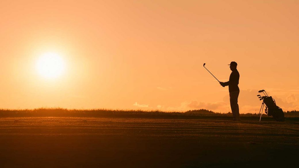 Silhouette of a man playing golf with a sunset in the background