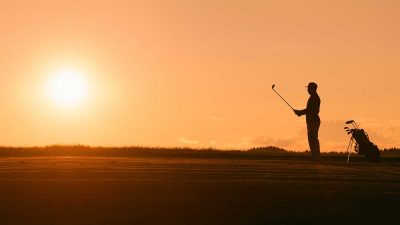 Silhouette of a man playing golf with a sunset in the background