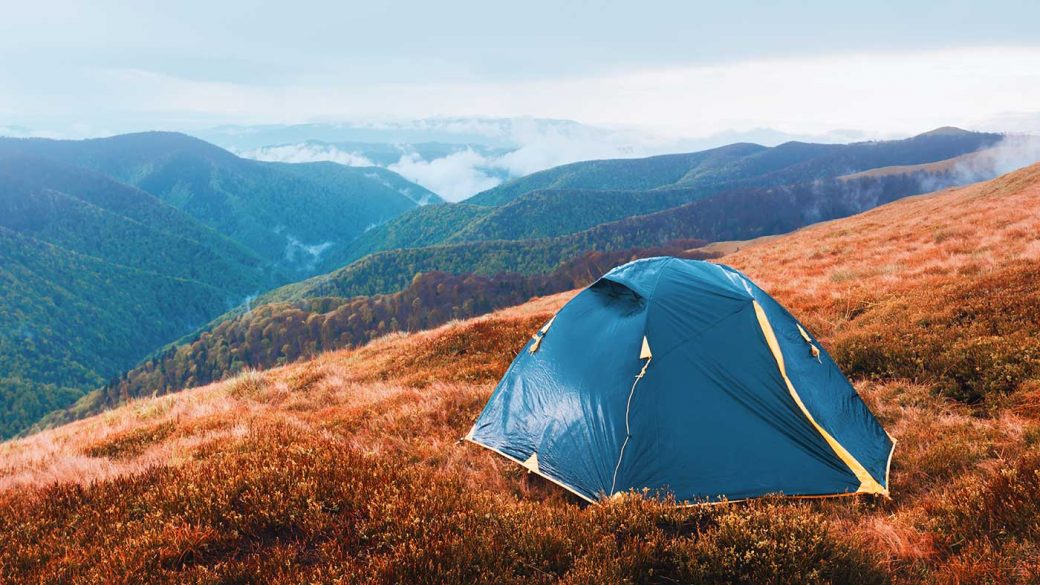 Tent pitched on mountain during autumn with tree covered mountains in background