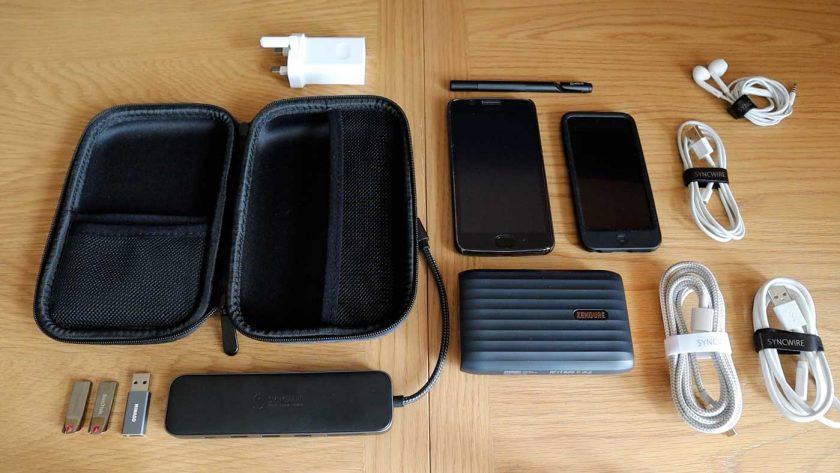 A selection of small electronics, cables and tech accessories layed out on a table next to the Syncwire travel case
