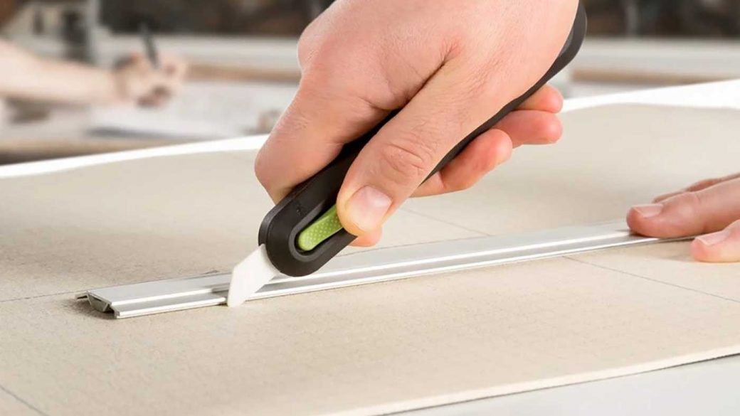 Person using a metal ruler and an auto-retractable utility knife to precision cut cardboard