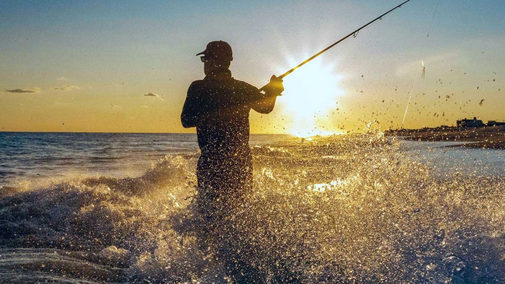 Fisherman standing knee-deep in the sea while fishing for bass at sunset