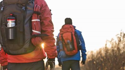 Two hikers wearing winter hiking gear and carrying backpacks with rope