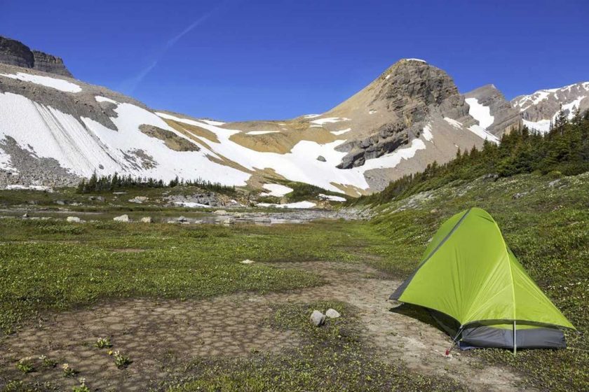 A green tent pitched in the wilderness in front of snow-capped mountains