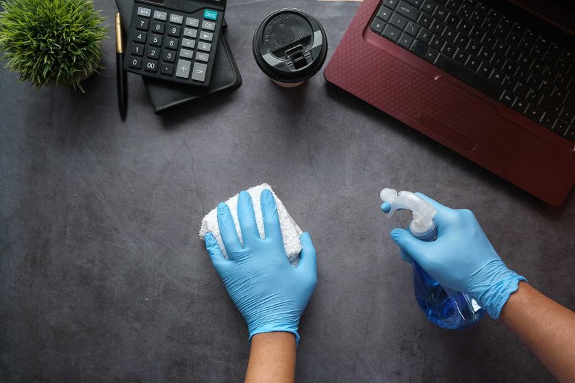 Person cleaning a desk surface with a cloth and antibacterial spray