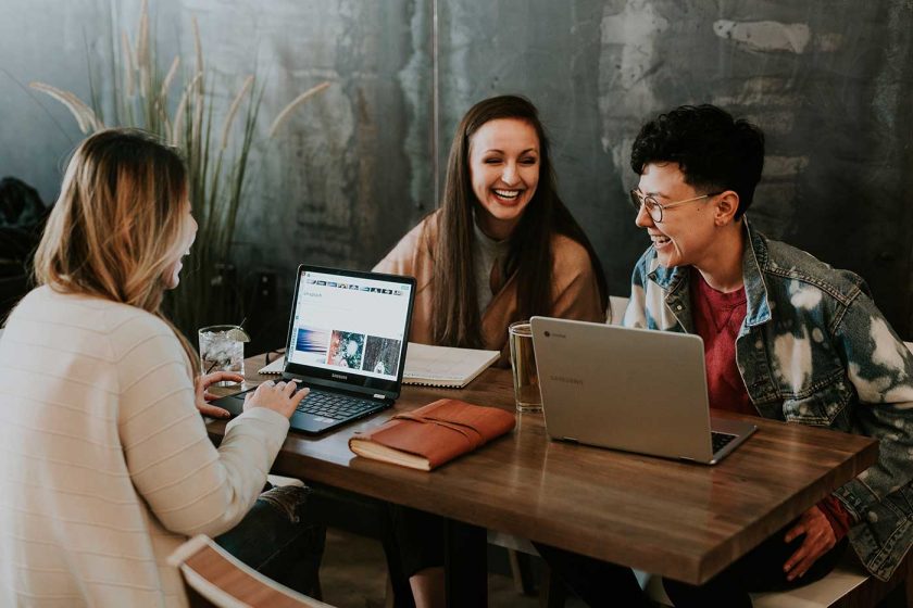 Three people working on laptops on the same table and laughing together