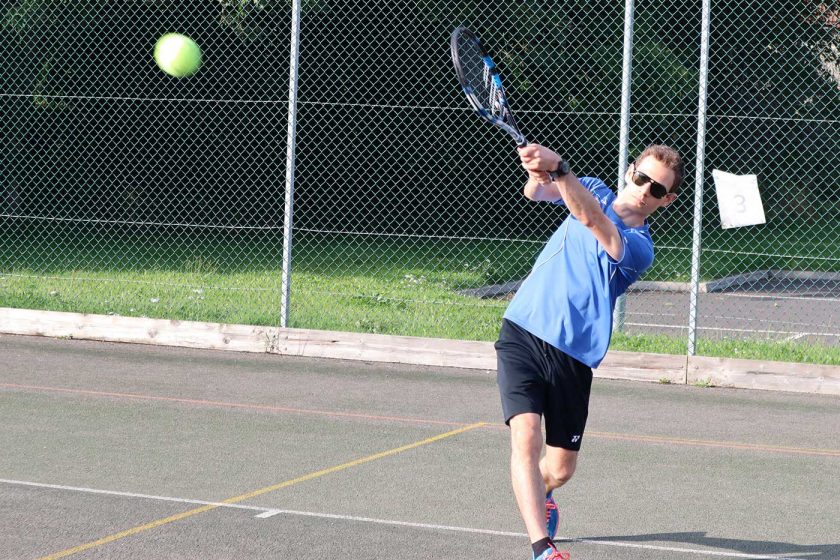 Playing a backhand tennis shot on an outdoor tennis court while wearing the Vallon Howlin’ sunglasses