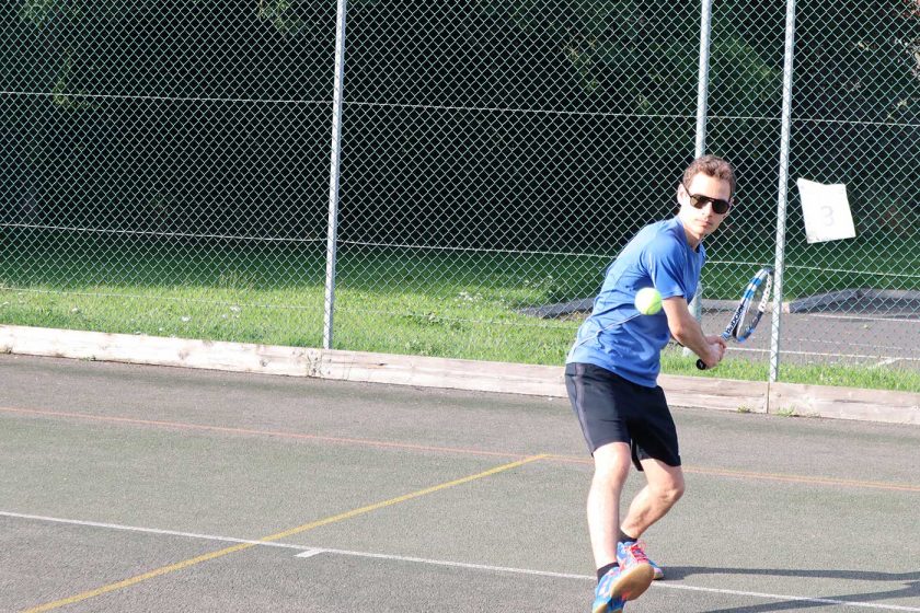 Preparing to play a backhand tennis shot on an outdoor tennis court while wearing the Vallon Howlin’ sunglasses