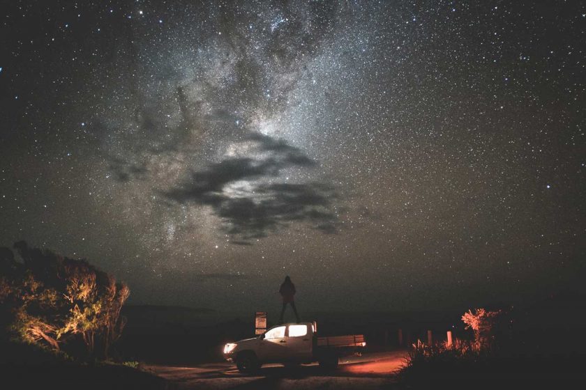 Traveller standing on top of a pickup truck under a starry night sky