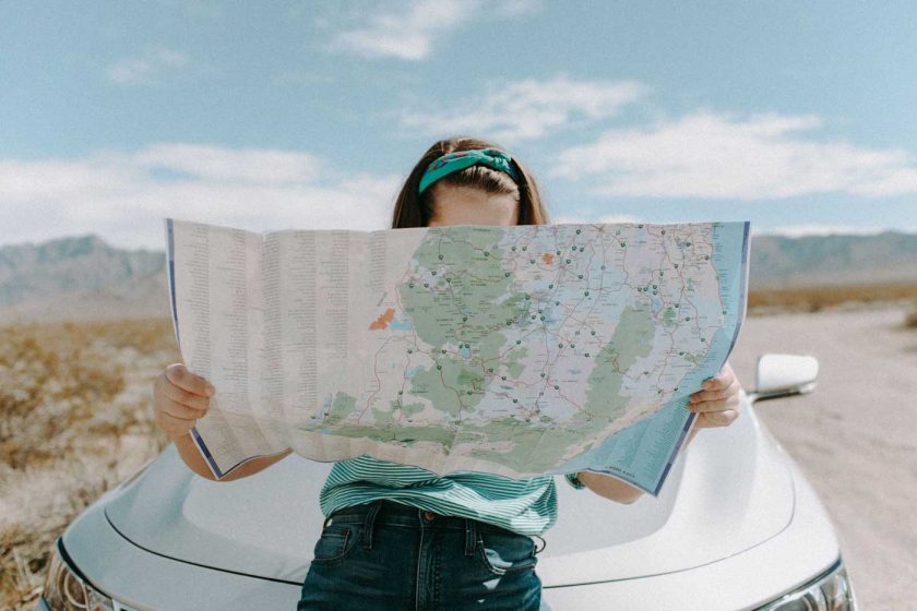 Woman sat on car bonnet reading a map