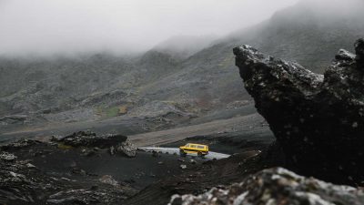 Yellow van driving on a mountain road under an overcast sky
