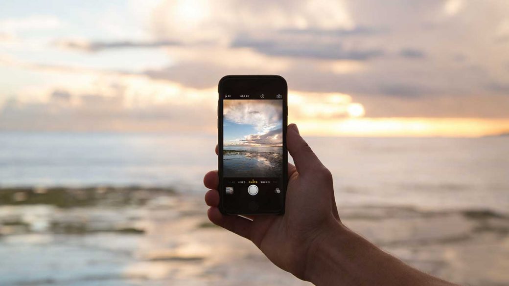 Person taking a photo of a sunset using a smartphone for social media