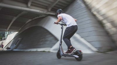 Man riding a kick scooter to work in order to beat the traffic and not be late