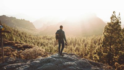 Hiker looking at a forest from a viewpoint while carrying a backpack and camera