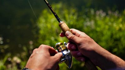 Fisherman reeling in a black and gold fishing rod with wooden handle