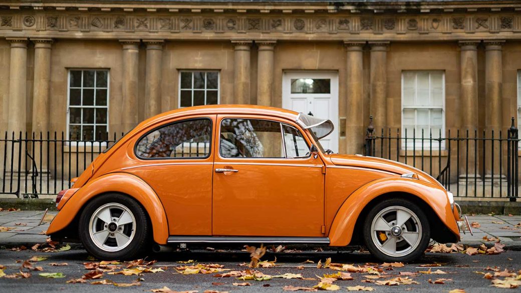 Classic orange Volkswagen Beetle parked in front of Georgian building in Bath, UK