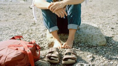 Woman sat on the beach, styling brown sandals with blue denim shorts