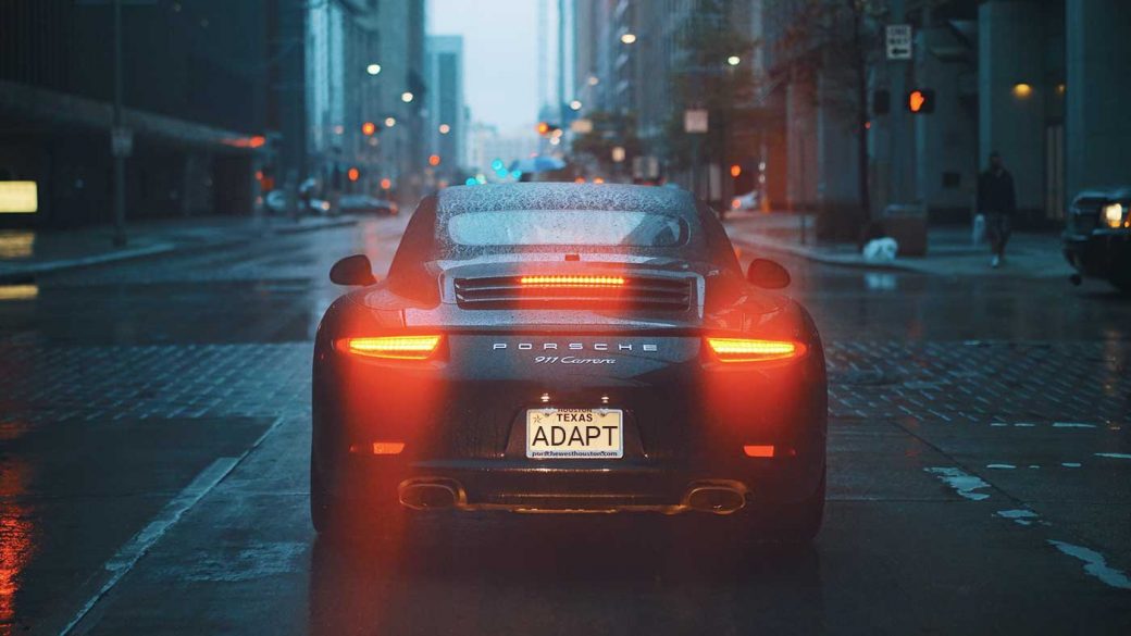 Gray Porsche 911 in wet city street with braking lights illuminated