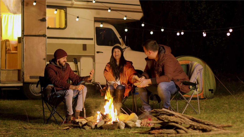 Friends sat around a camp fire in camping chairs