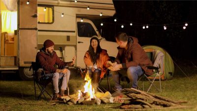 Friends sat around a camp fire in camping chairs