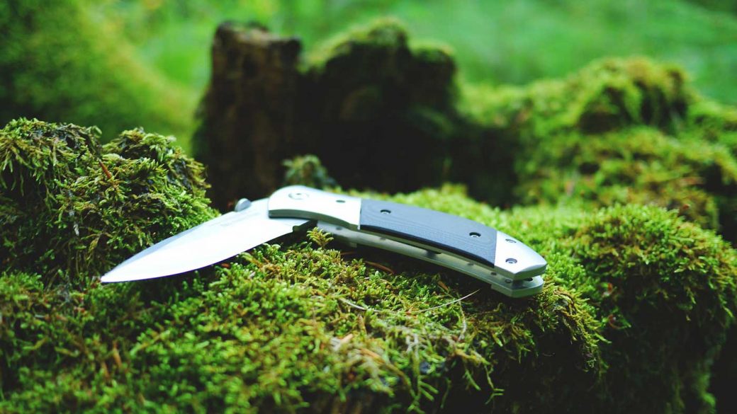 Folding survival knife on moss covered log