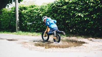 Toddler riding a balance kid’s bike through a puddle