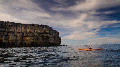 Man ocean kayaking next to cliffs
