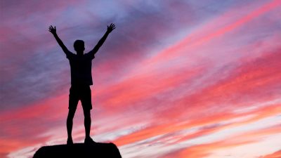 Silhouette of man standing on rock with his arms in the air in front of sunset