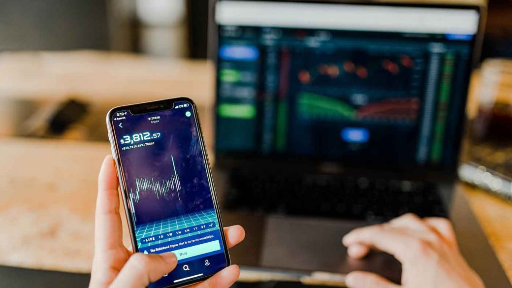 Person using an online investment broker on their phone and laptop