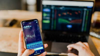 Person using an online investment broker on their phone and laptop