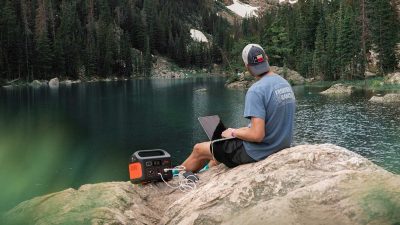 Man sitting by a lake using a portable generator to power his laptop