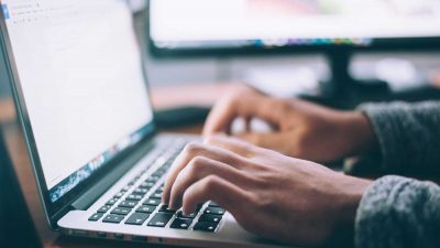 Job seeker writing their resume on a laptop using a resume writing guide