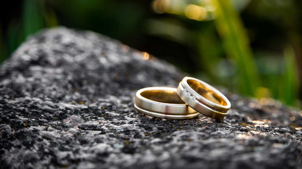 A pair of gold wedding rings sitting on a rock